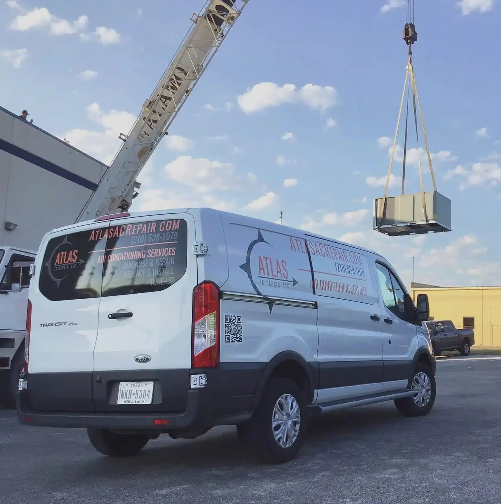 An Atlas AC Repair van beside a crane lifting a rooftop HVAC unit