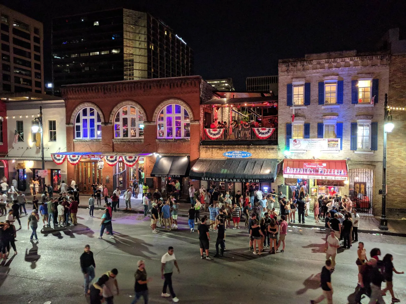 Crowds walk past illuminated bars on Sixth Street in downtown Austin at night