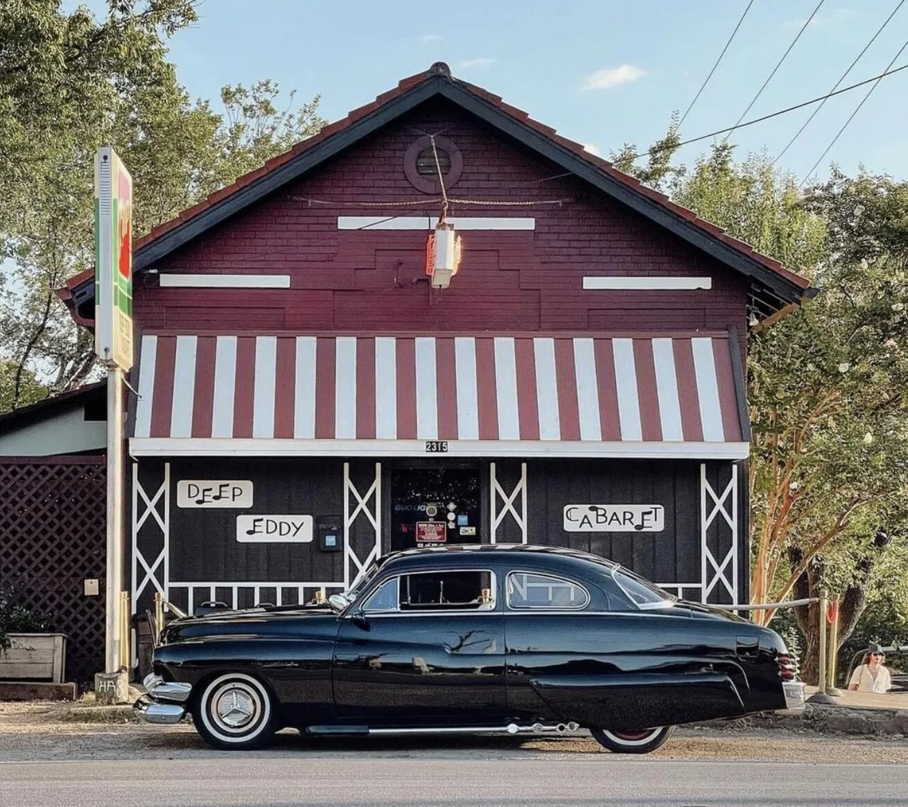 A vintage black car parked in front of Deep Eddy Cabaret's striped facade