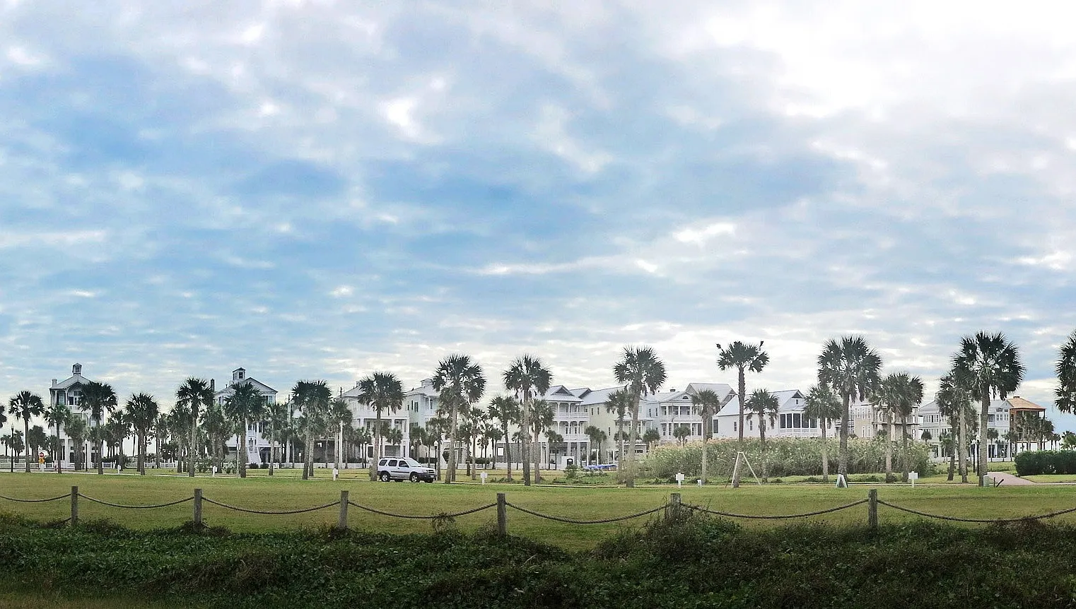 Stilt houses standing beyond grass-covered dunes at Galveston's East Beach