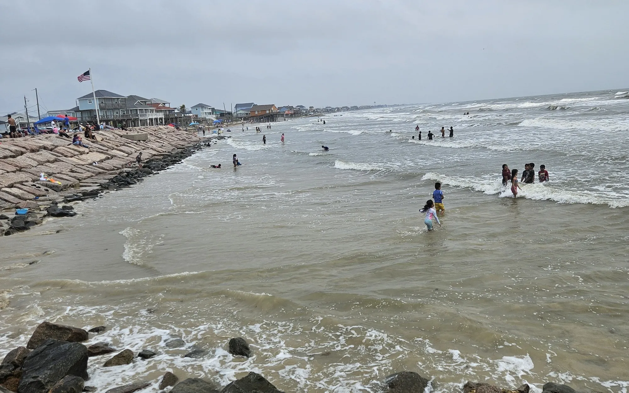 People wading beside a rock jetty in the choppy Gulf at Surfside Beach