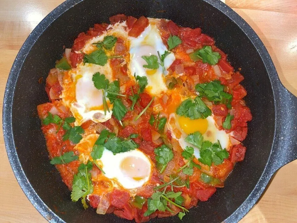 Shakshuka with eggs poached in tomato and onion sauce, topped with cilantro