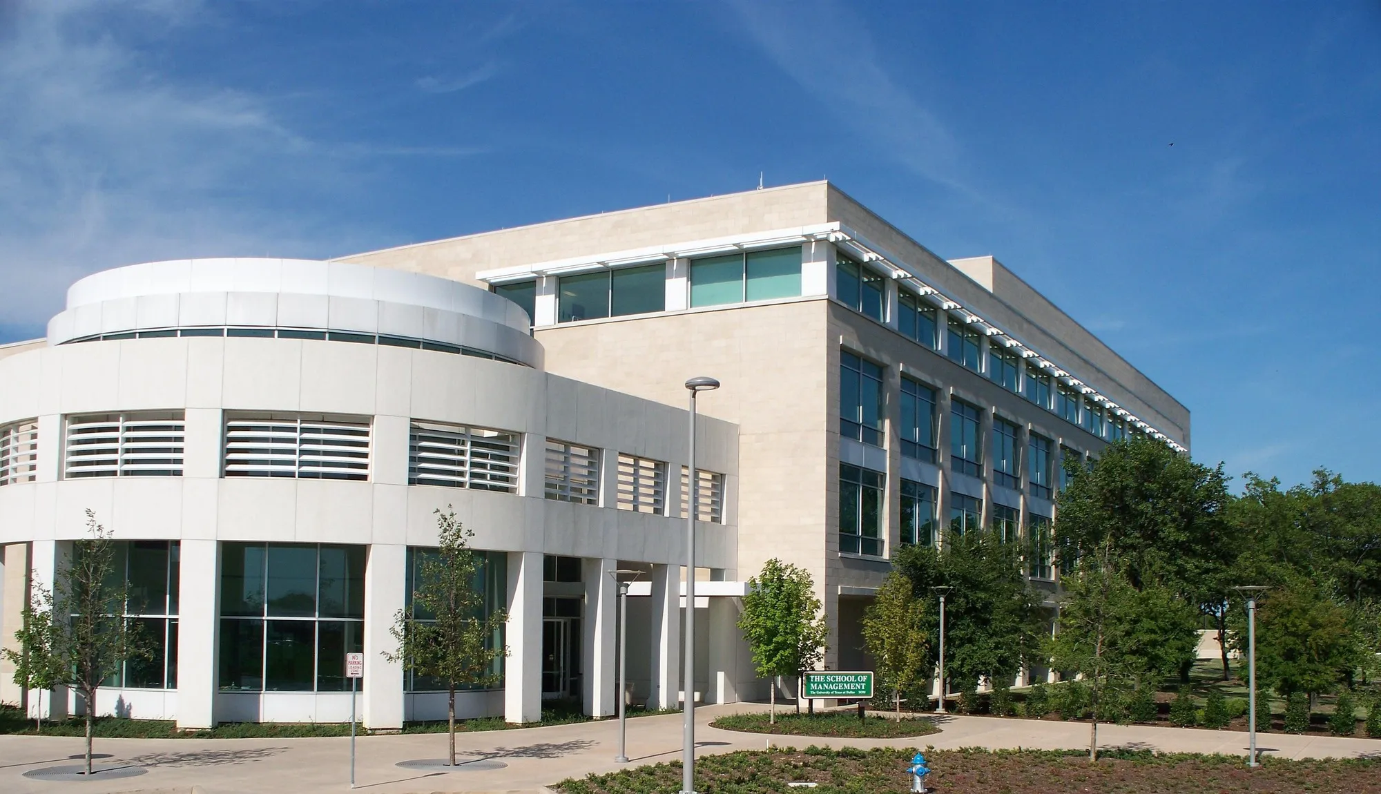 The curved white facade and glass windows of the UT Dallas School of Management building