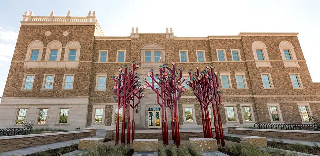 The brick Rawls College of Business facade behind red tree-shaped sculptures at Texas Tech