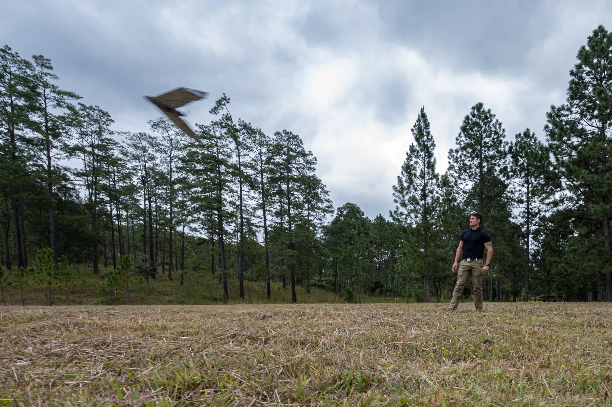 A technician in safety gear launching a fixed-wing survey drone over open terrain