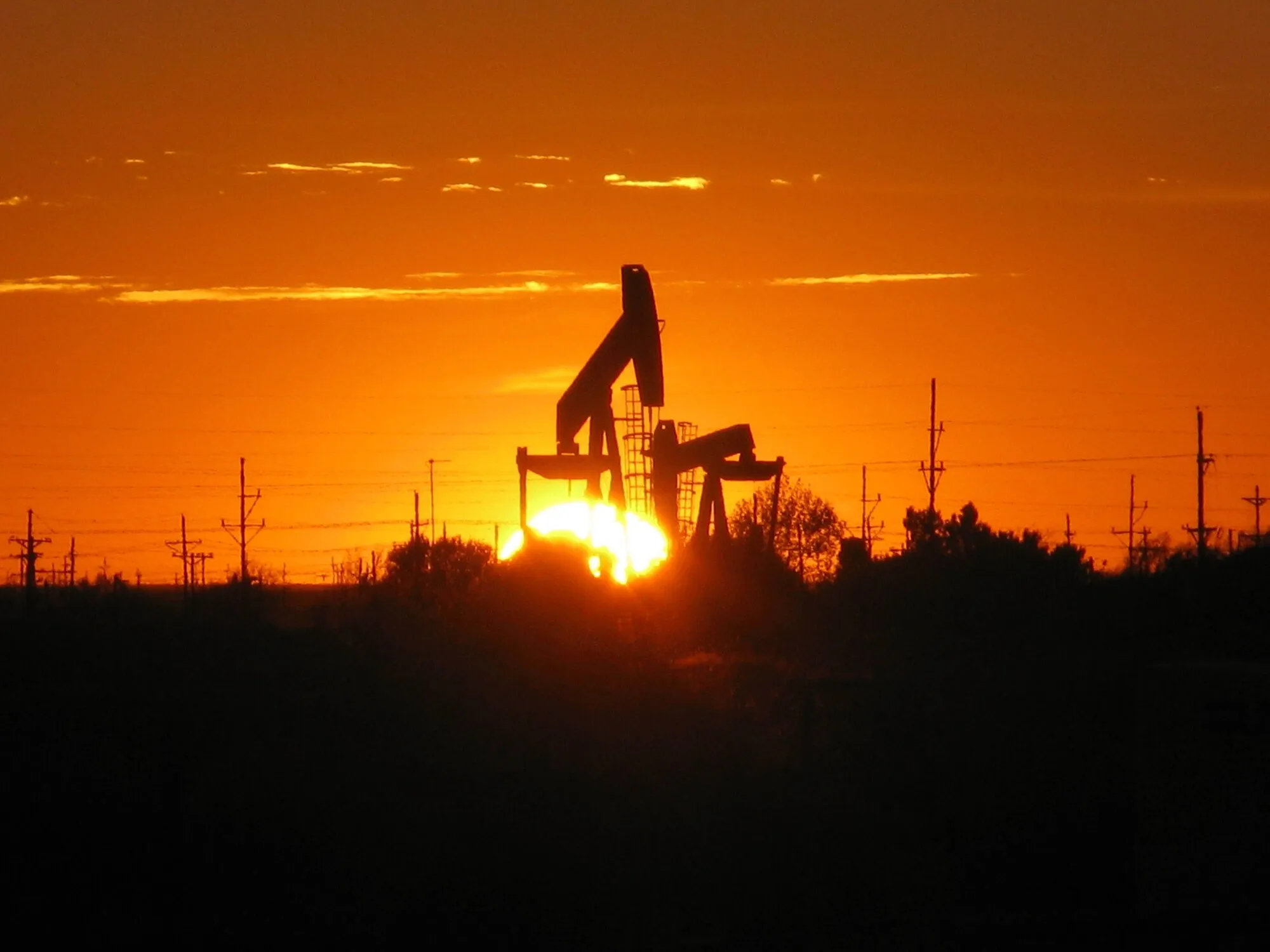 A pump jack silhouetted against an orange West Texas sunset