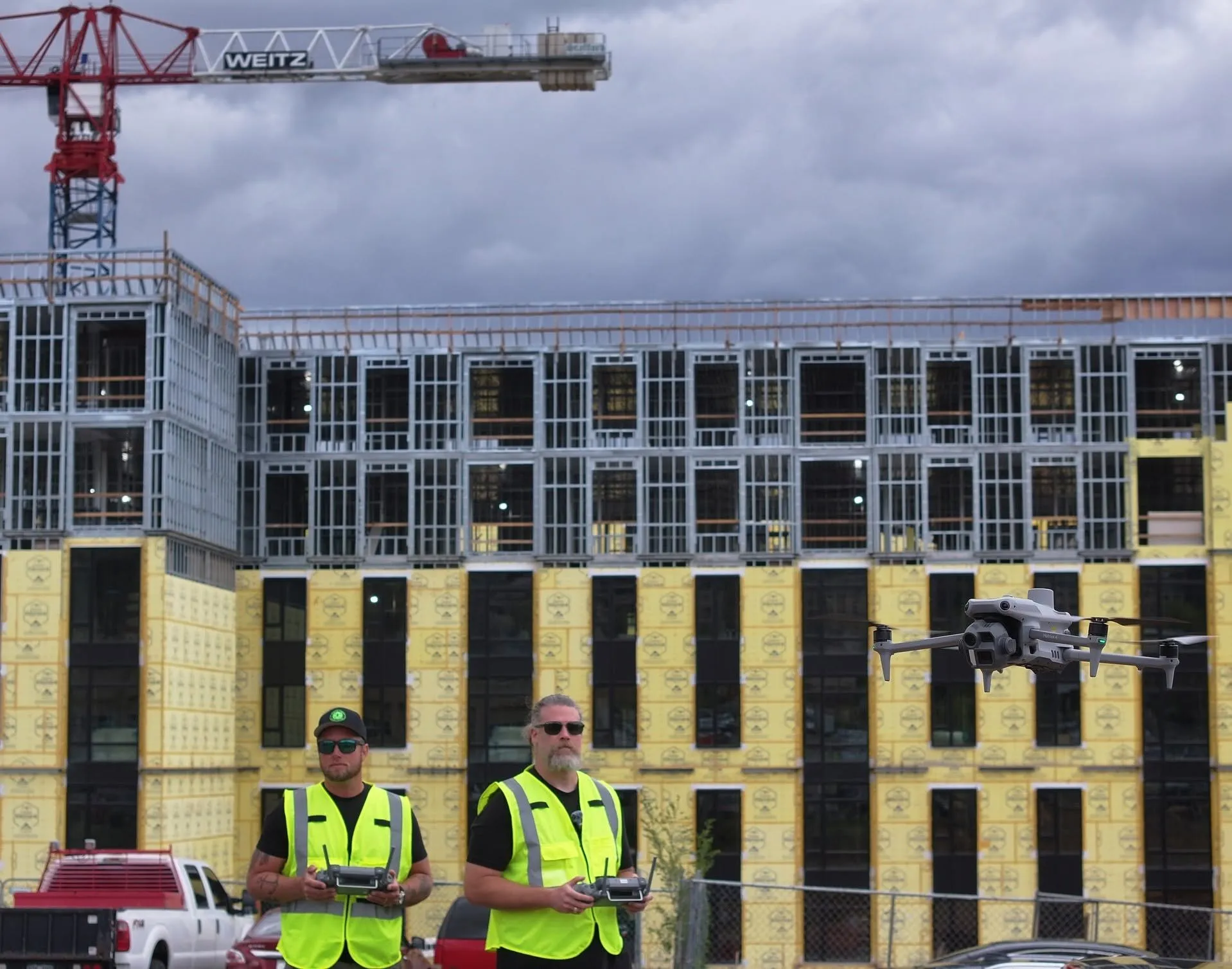 Two Skyline Drone Mapping pilots controlling a quadcopter in front of a multistory construction project