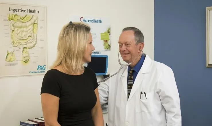 James Maher, MD, uses a stethoscope beside a woman in a medical office