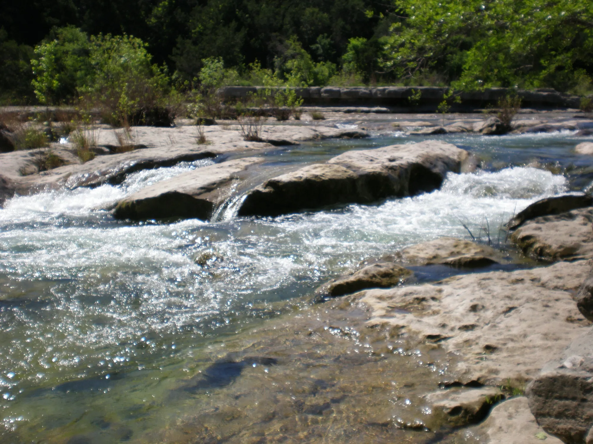 Water rushing over low limestone ledges on Barton Creek Greenbelt during the rainy season