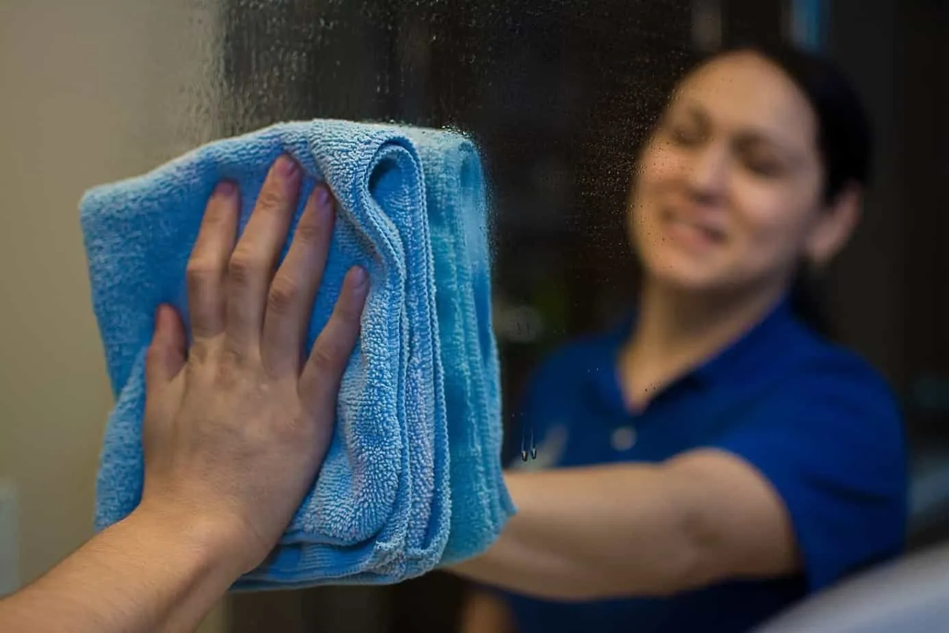 A Bee Maids cleaning technician wiping a glass surface with a blue microfiber cloth