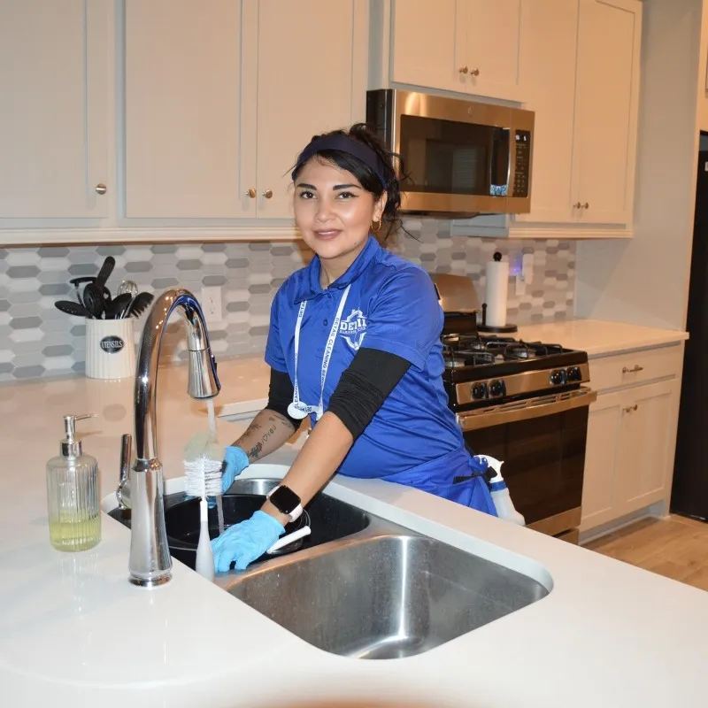 A Detail Cleaning Services technician in a blue branded uniform washing utensils at a kitchen sink