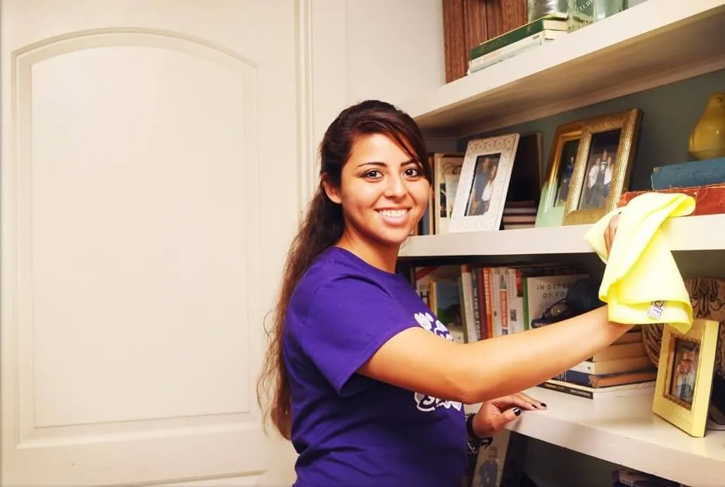 Naturalcare founder Lupe wiping a shelf while wearing the company's purple uniform shirt