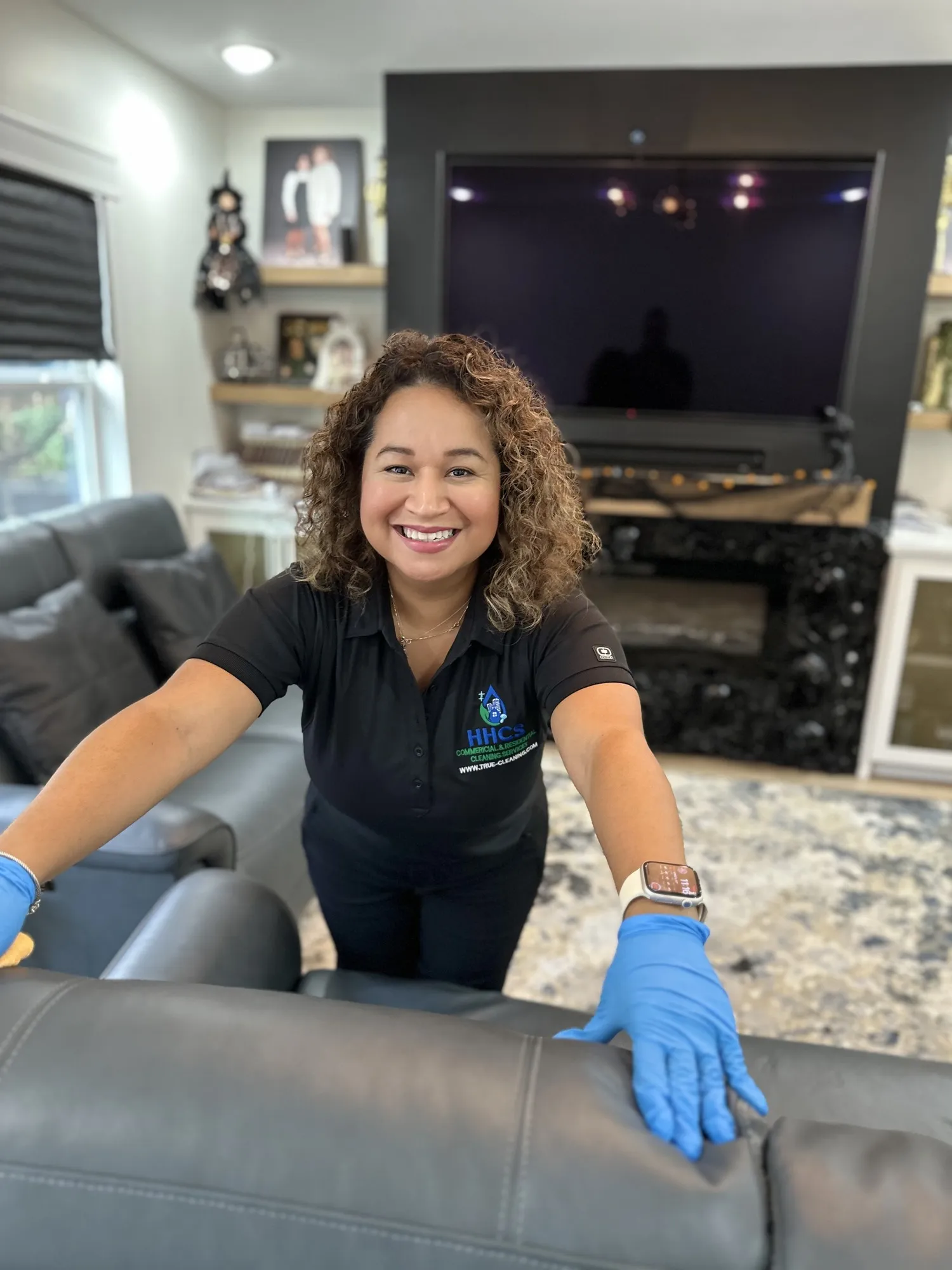 A Healthy Home Cleaning System technician in a branded polo and blue gloves wiping a leather sofa