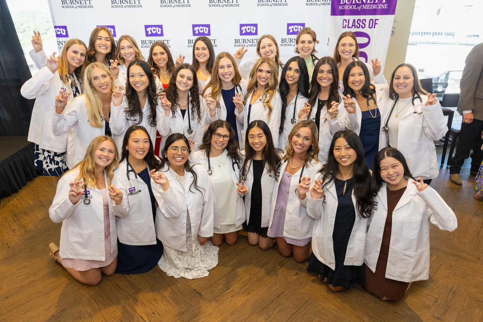 Burnett School of Medicine students pose together in white coats before a TCU Class of 2030 backdrop