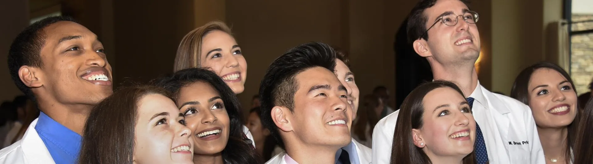 Baylor College of Medicine students in white coats smiling and looking toward a stage