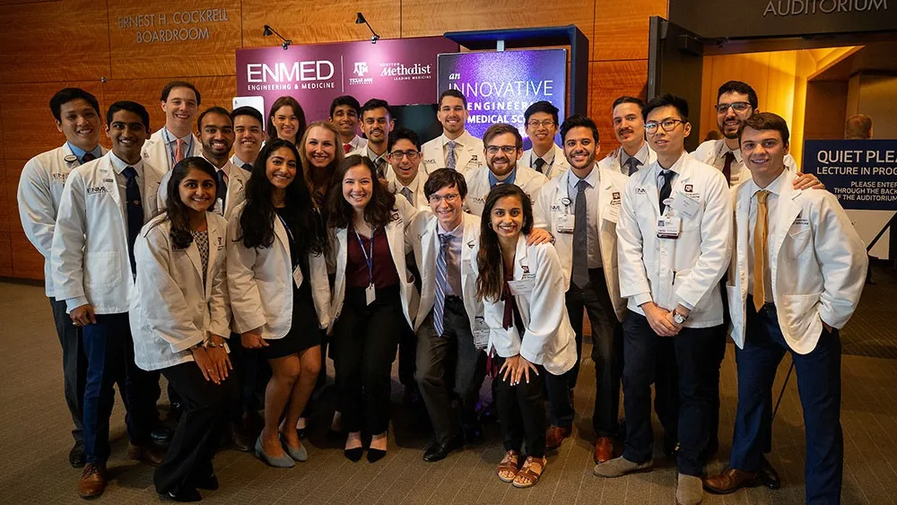 The inaugural EnMed class posing in white coats beside Texas A&M and Houston Methodist signs