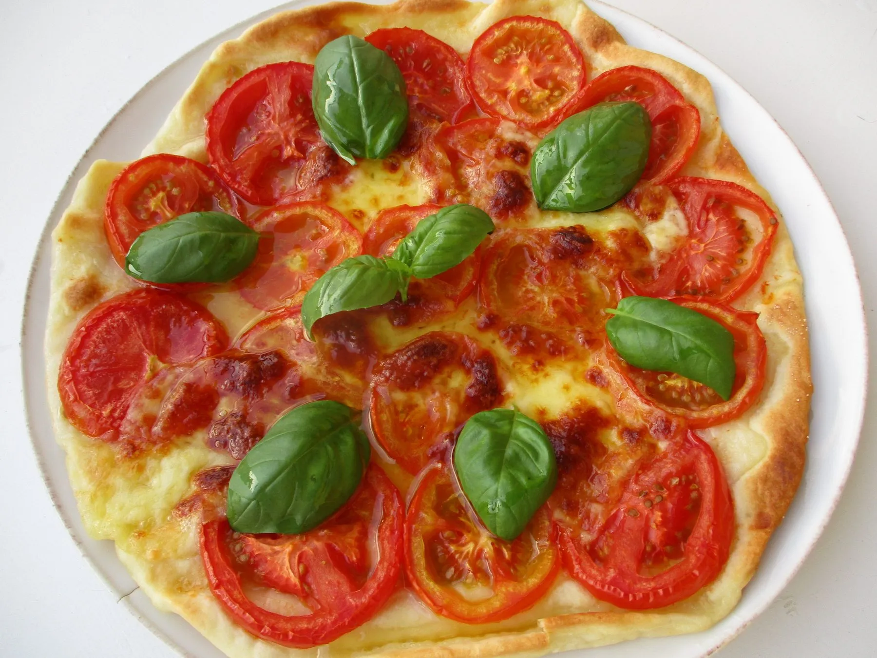 A margherita pizza topped with sliced tomatoes, mozzarella and basil