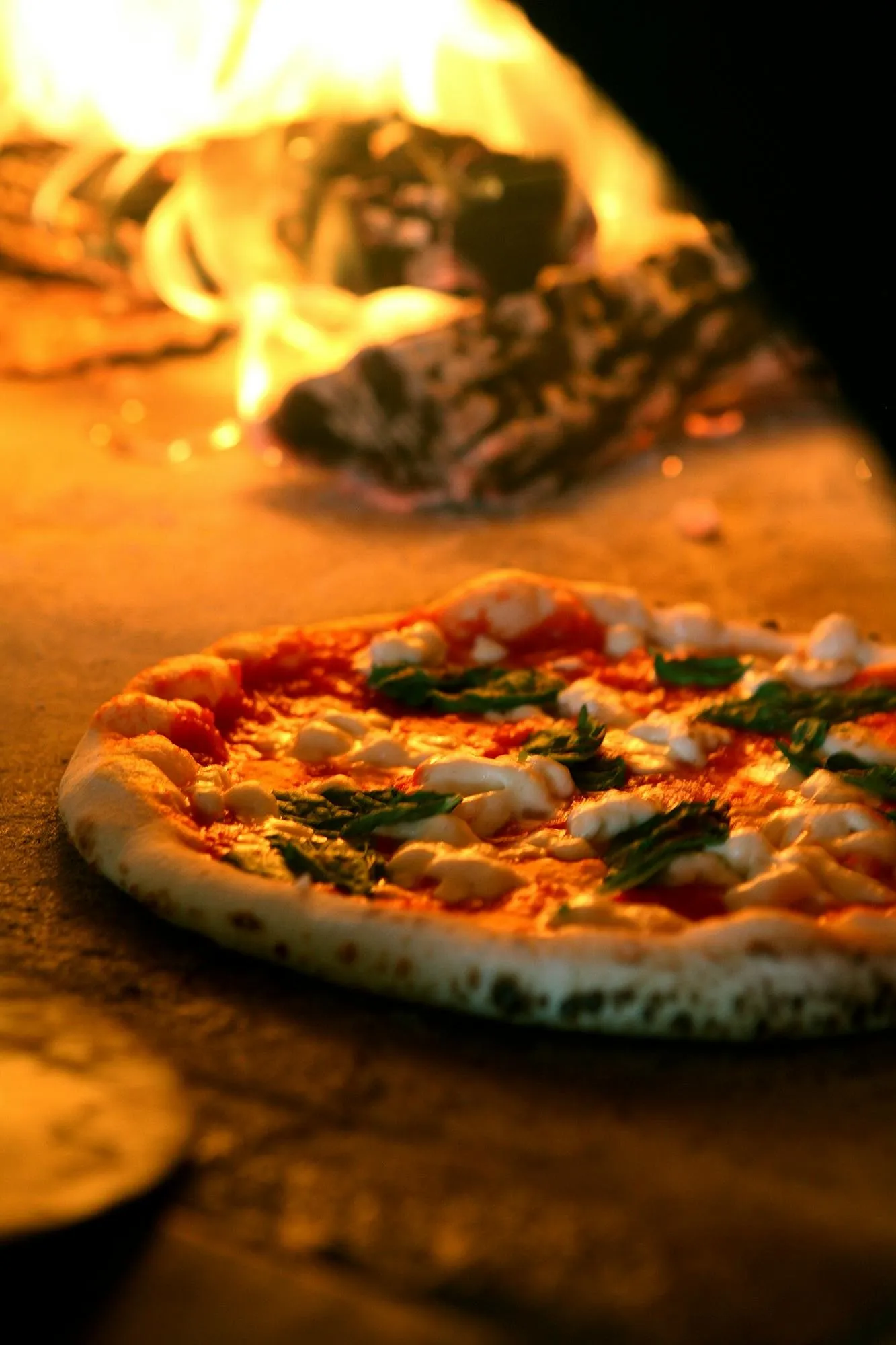 A Margherita pizza baking beside the flames in one of Dough Pizzeria Napoletana's wood-fired ovens