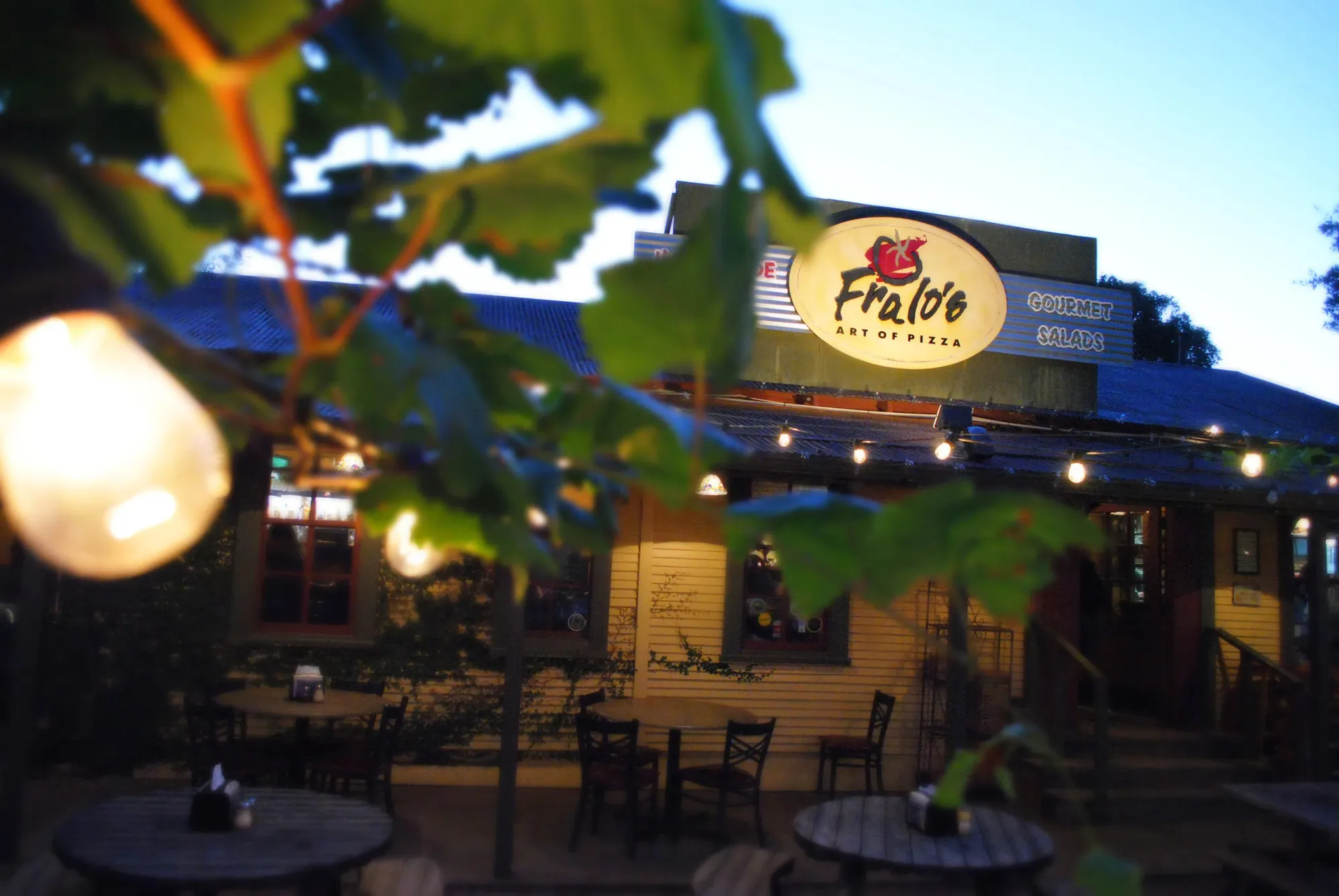 Fralo's Art of Pizza exterior and patio at dusk, with its illuminated sign above the entrance
