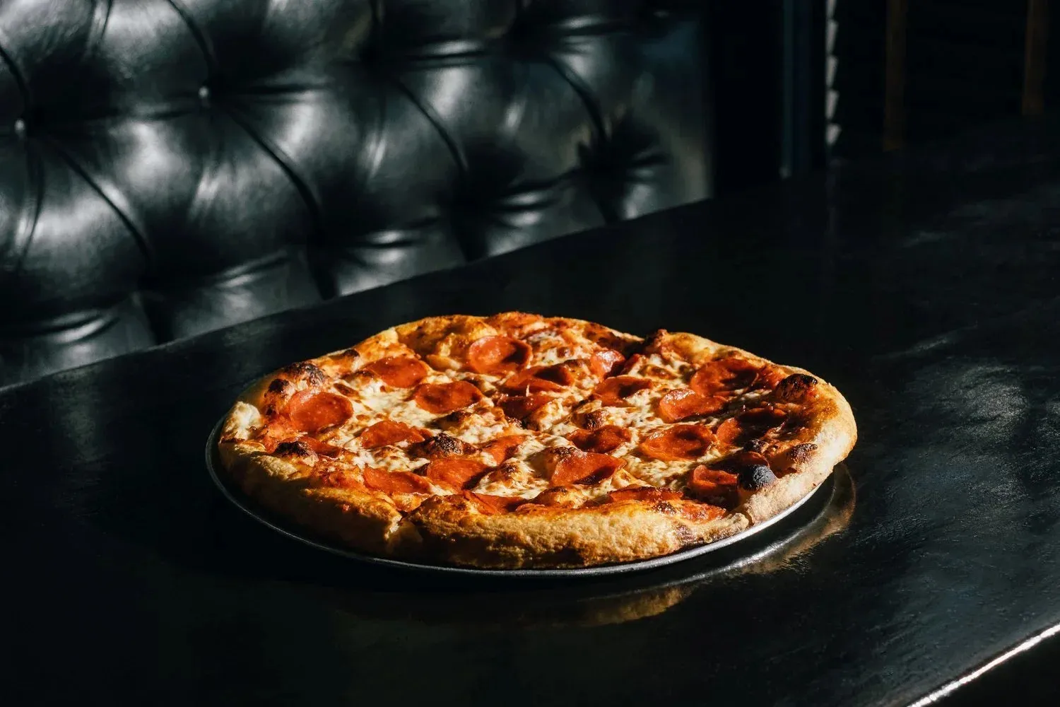 A Barbaro pizza on a dark table against the restaurant's black leather banquette