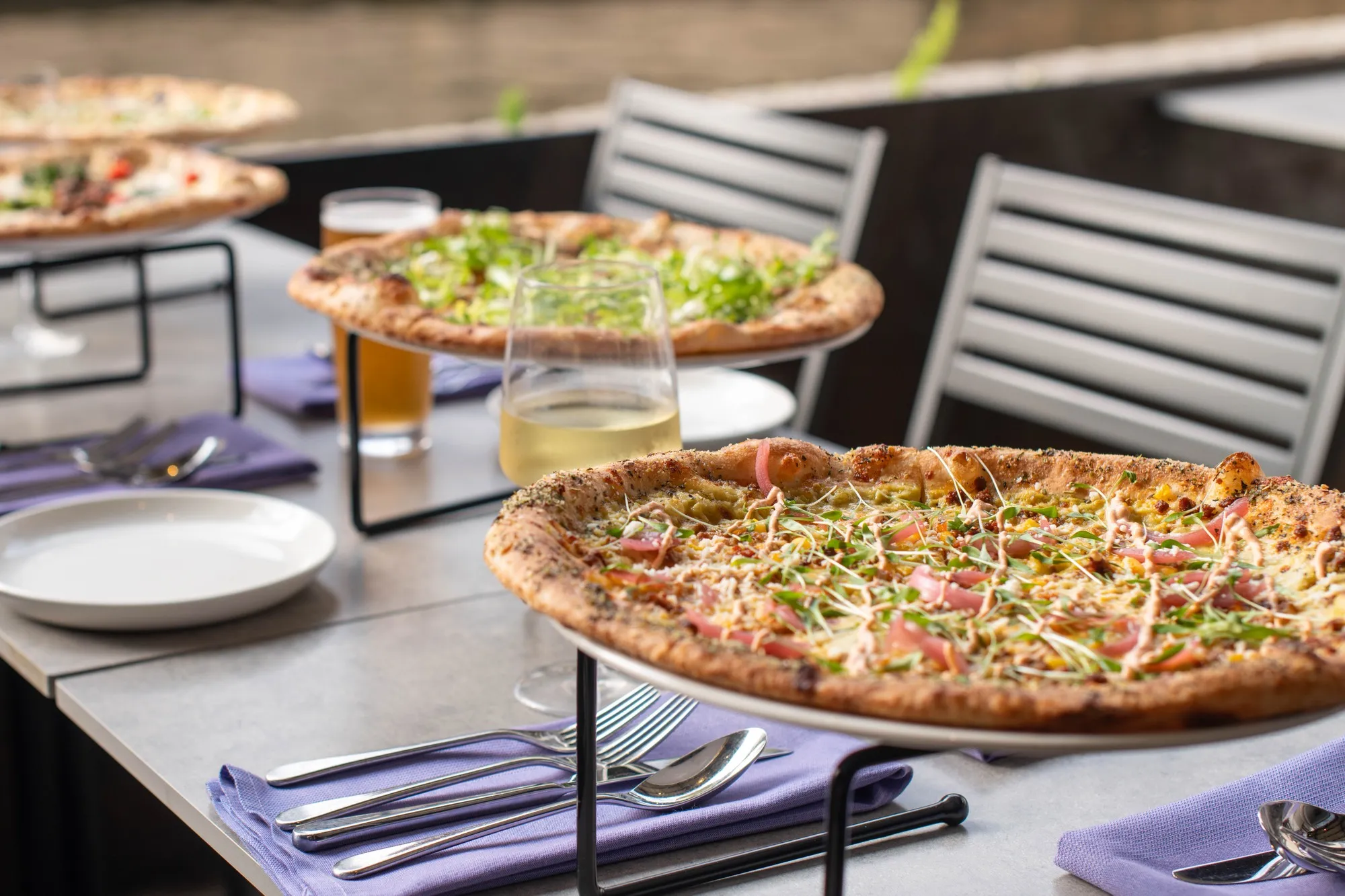 Several Fiume pizzas on raised trays across an outdoor dining table