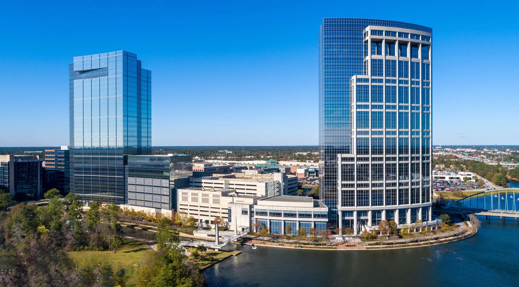 Office towers rising above the tree line along The Woodlands Waterway