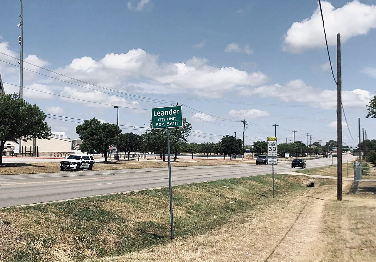 A Leander city-limit sign beside a road under a blue Texas sky