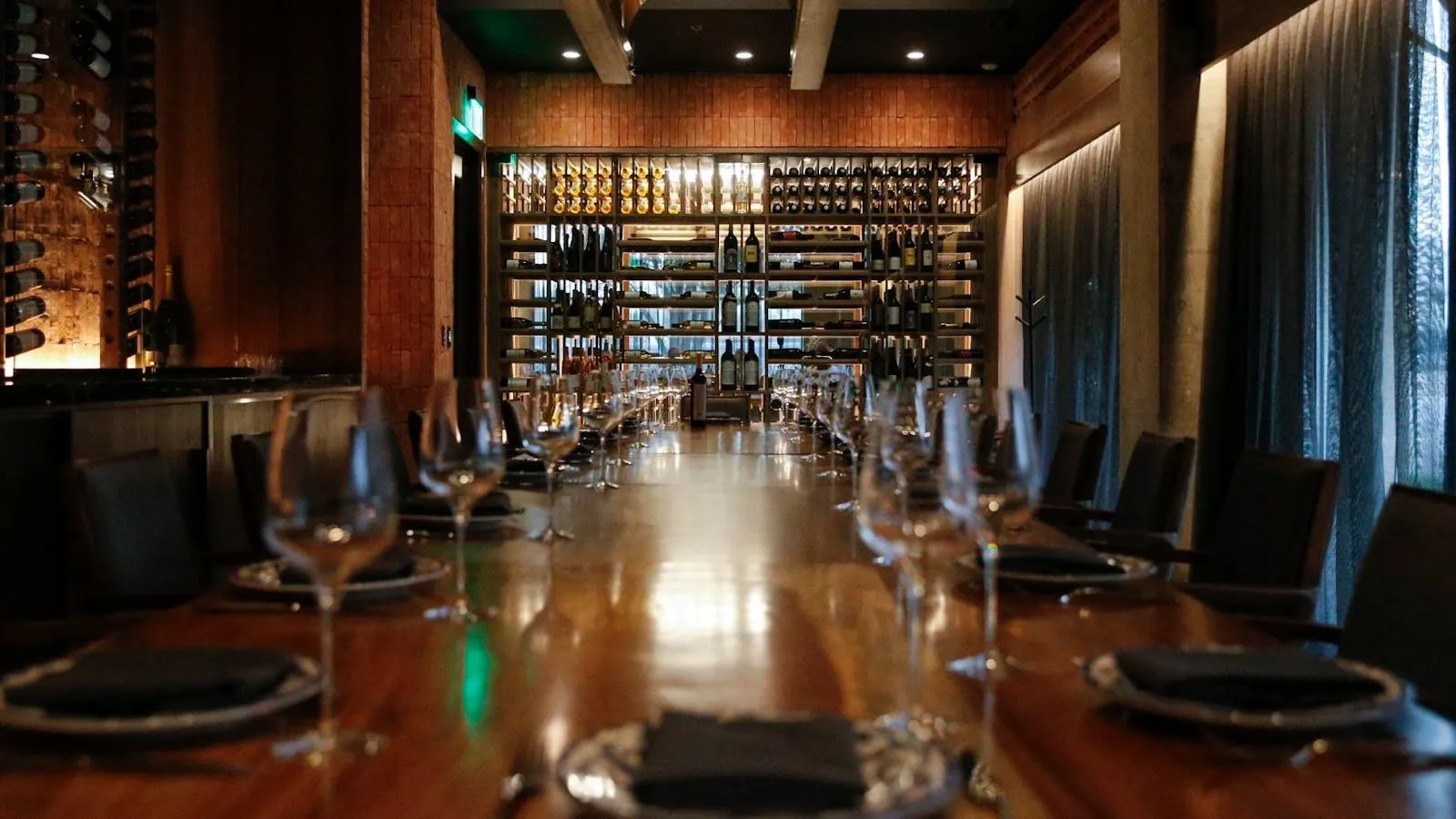 A long private dining table set with wine glasses in front of Don Artemio's illuminated wine wall