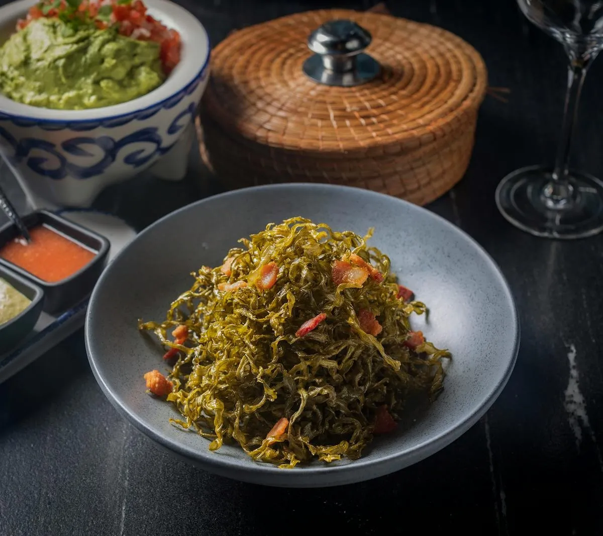 A colorful plated entrée with greens and vegetables on a dark table at Don Artemio