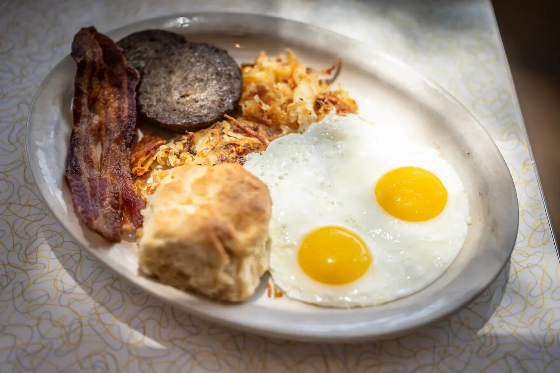 Two fried eggs with bacon, sausage, hash browns, and a biscuit at Paris Coffee Shop