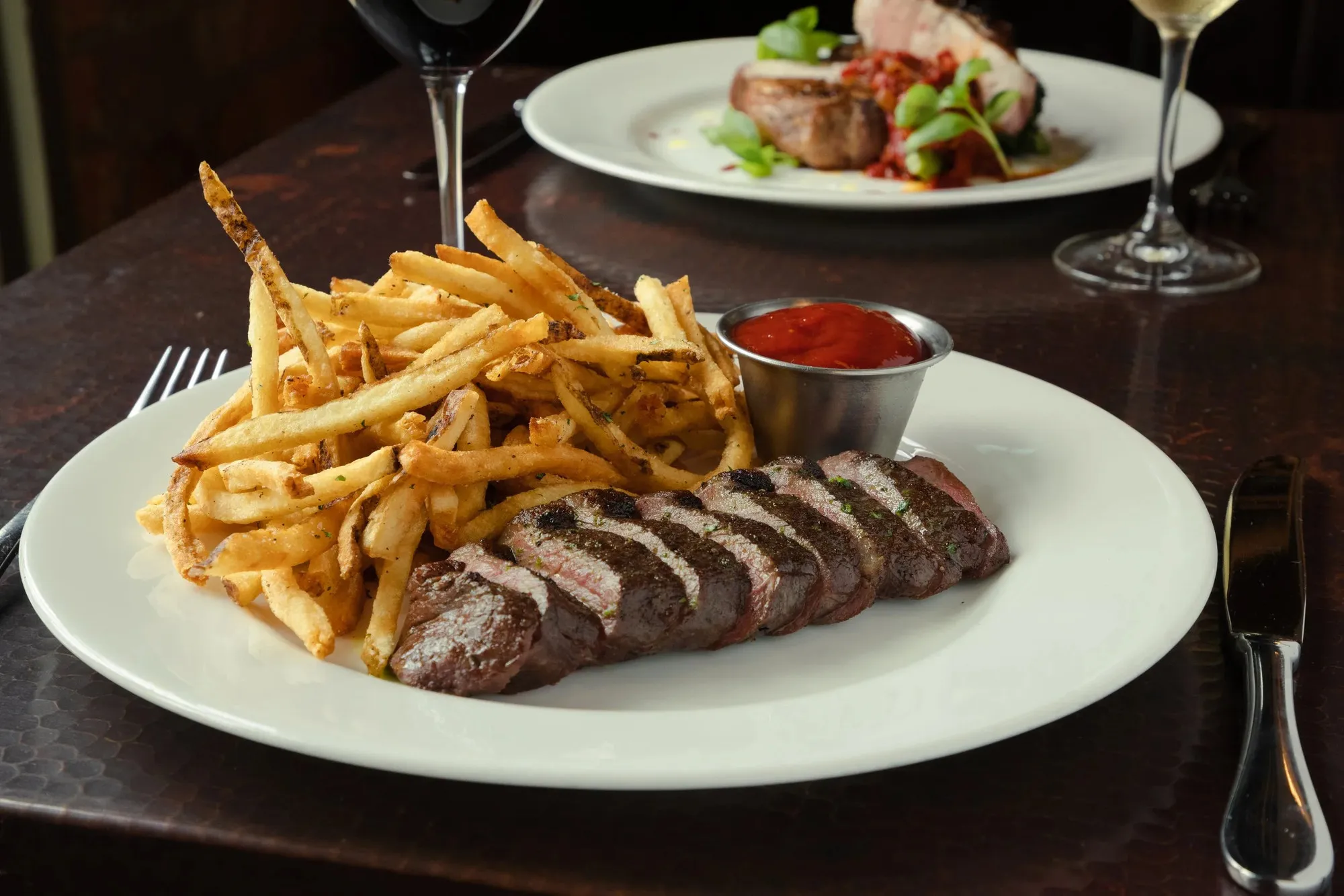 Sliced steak with thin fries and ketchup on a white plate at Clay Pigeon
