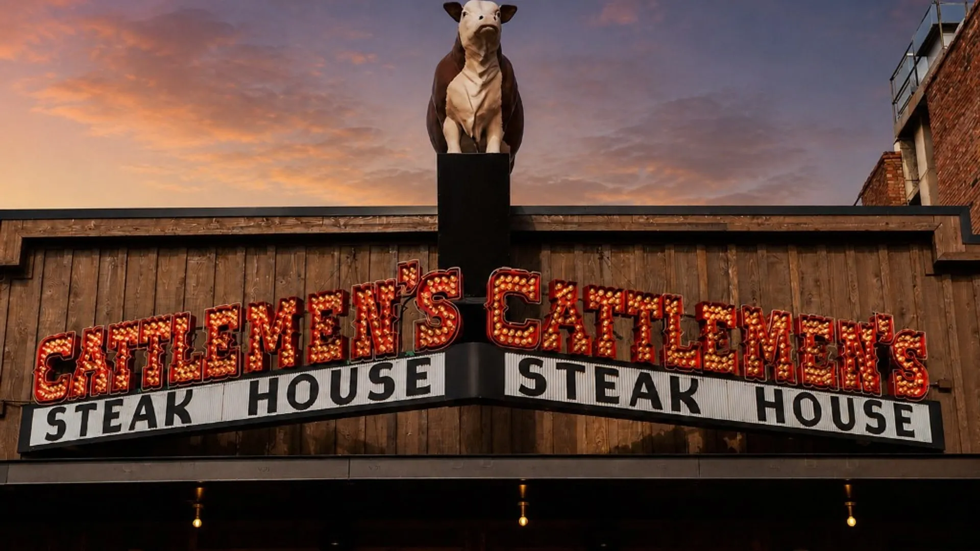 The illuminated Cattlemen's Steak House sign and rooftop steer beneath a sunset sky