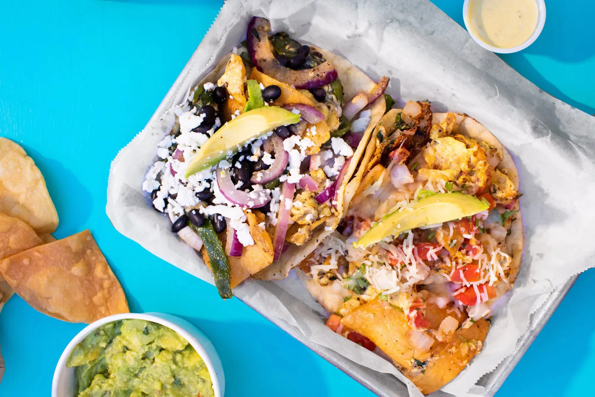 An overhead Veracruz All Natural spread with tacos, chips, guacamole and salsa on a turquoise table