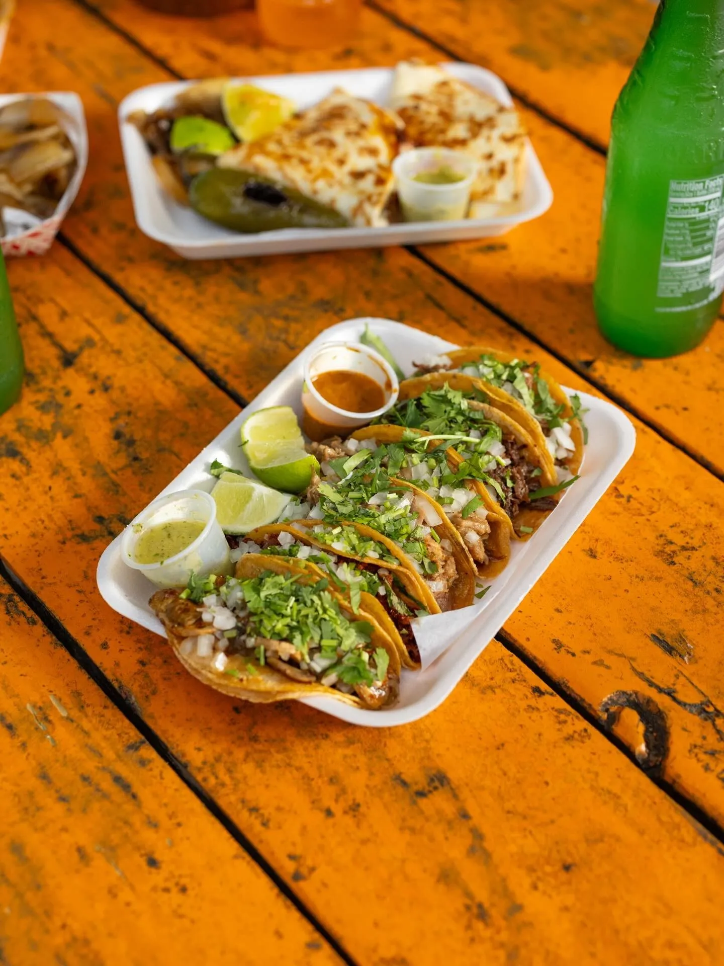 A tray of small Cuantos Tacos topped with chopped onion and cilantro on an orange picnic table
