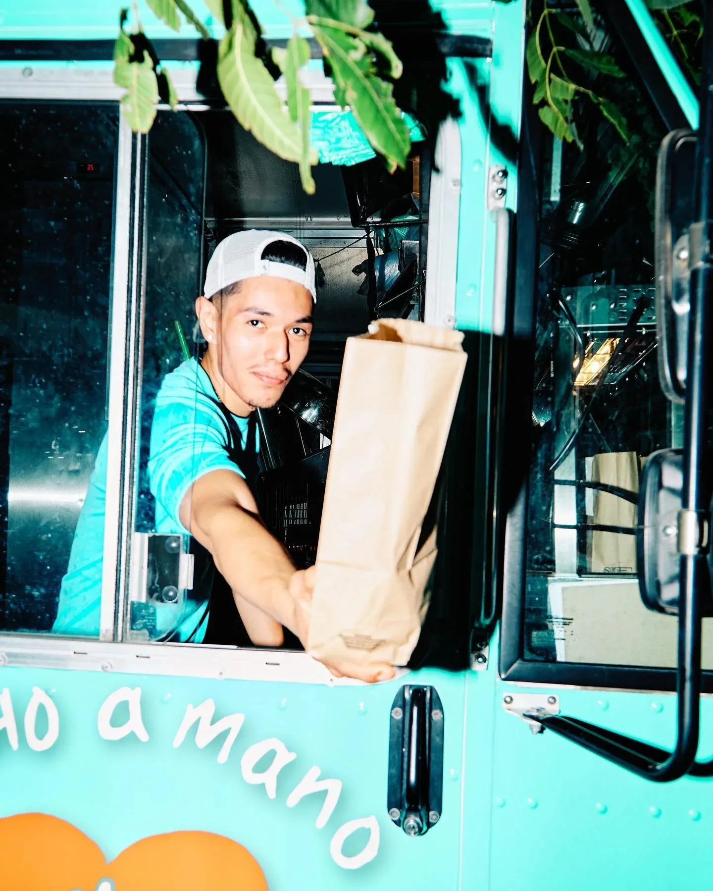 A Veracruz All Natural worker passing a brown paper takeout bag through a painted trailer window