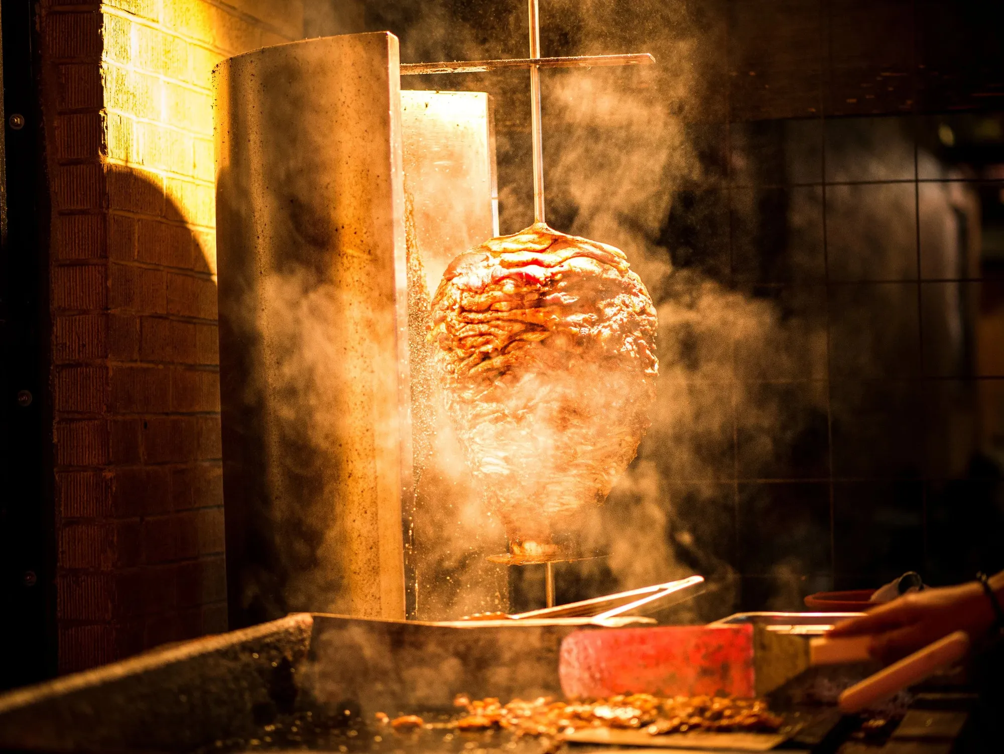 A vertical al pastor trompo roasting beside an open flame in the Vaquero Taquero kitchen