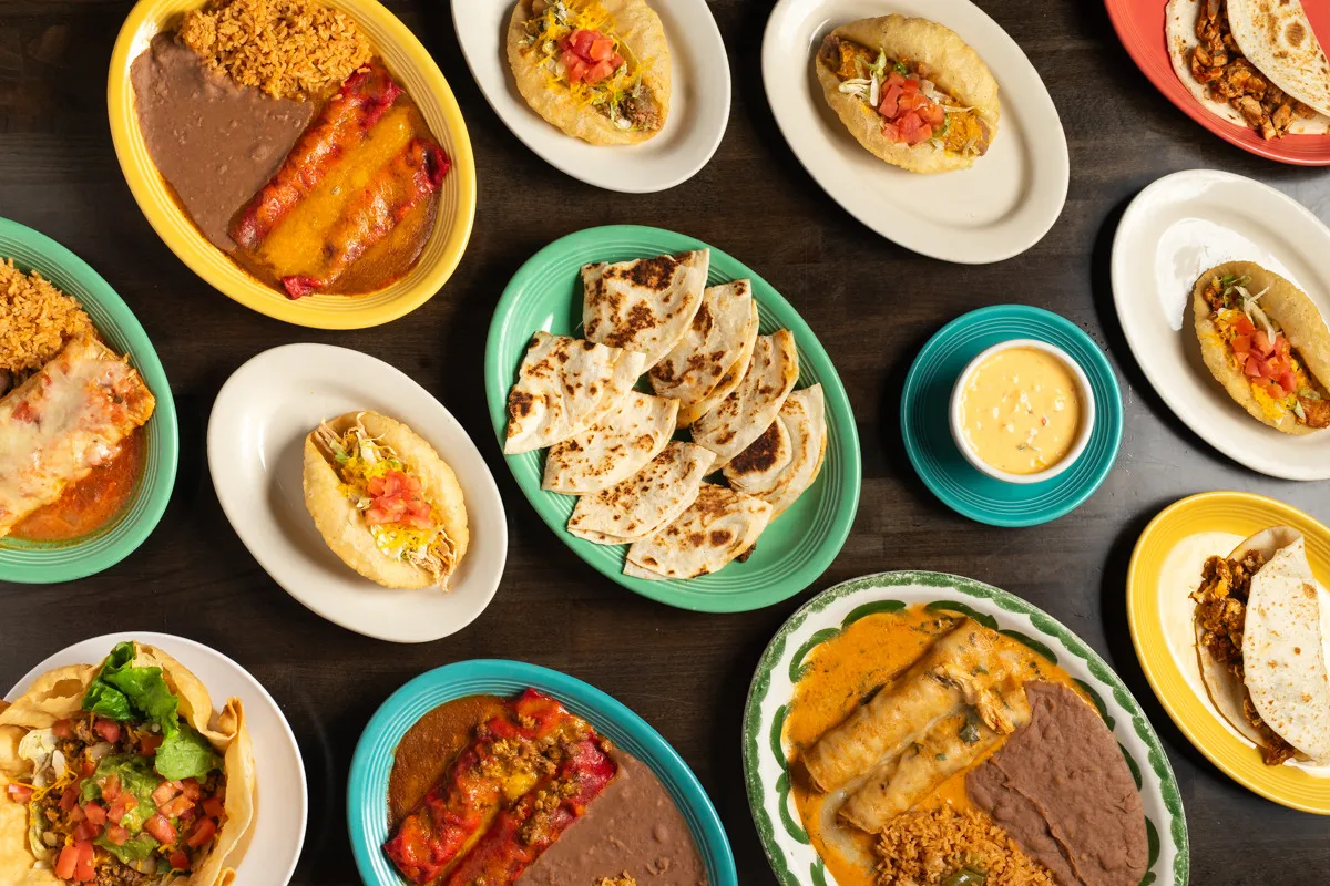An overhead spread of puffy tacos, enchiladas, rice, beans, and house tortillas at Henry's Puffy Tacos