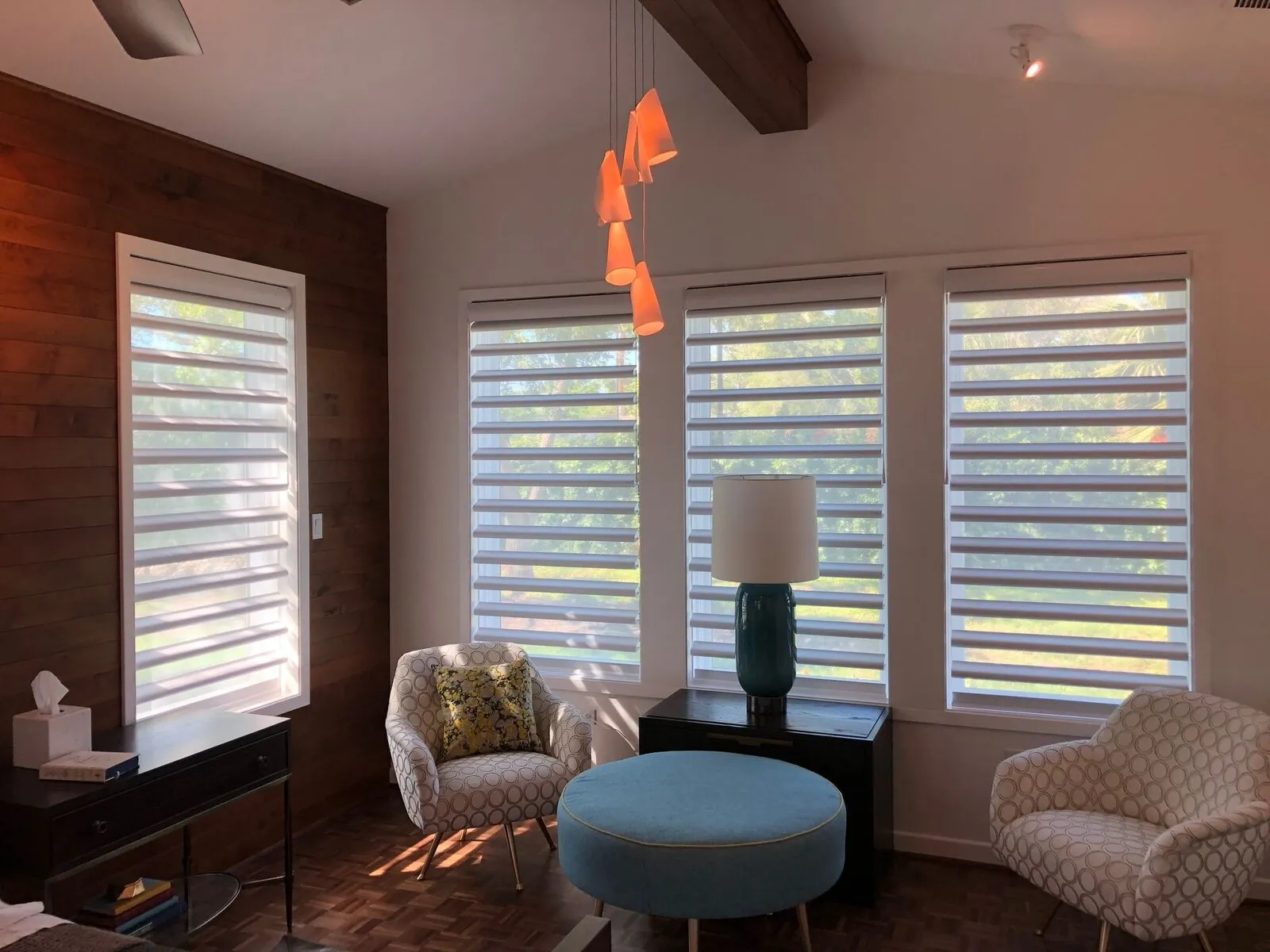 Pale layered window shades across a bank of tall windows in a furnished room
