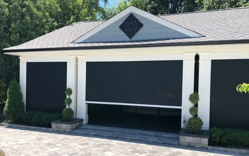 Black retractable screens covering the openings of a white outdoor pavilion