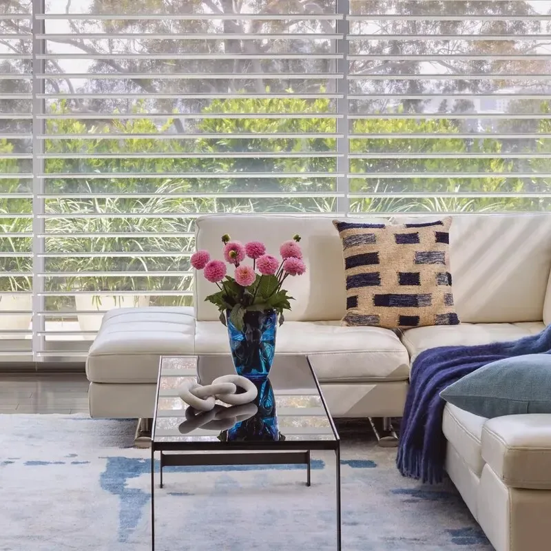 A bright living room with wide horizontal window shadings behind a white sofa