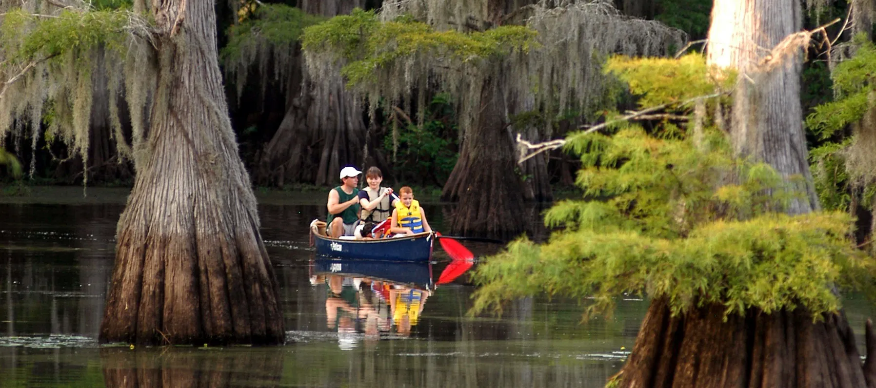 Visitors paddle a canoe among cypress trees at Caddo Lake State Park