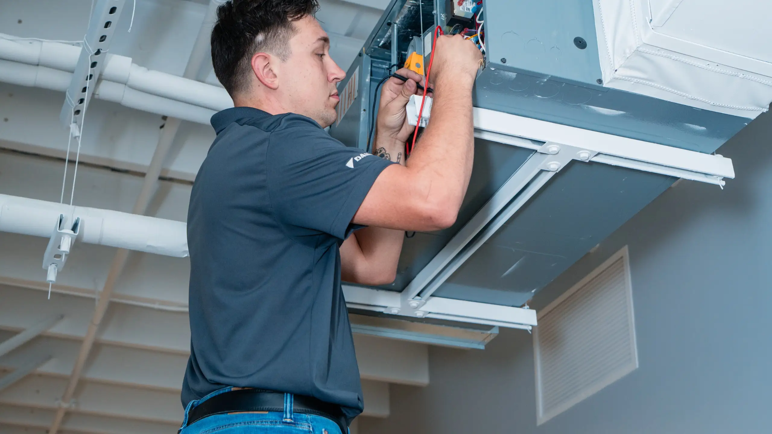 A Comfort-Air technician using a meter inside a ceiling-mounted HVAC unit