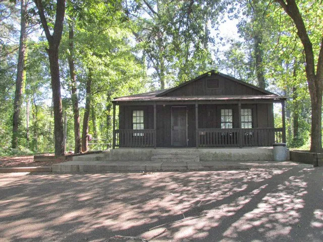 Wooden cabin with a screened porch beneath tall trees at Daingerfield State Park
