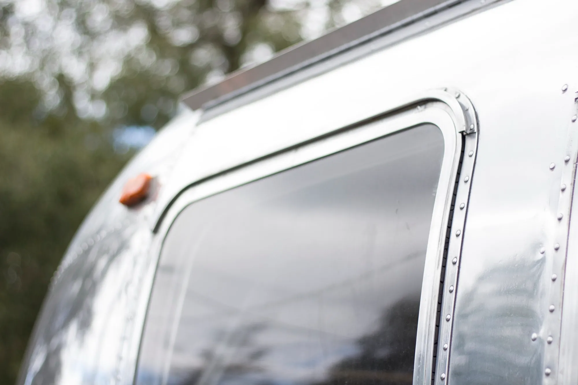 A polished silver travel trailer reflecting nearby trees