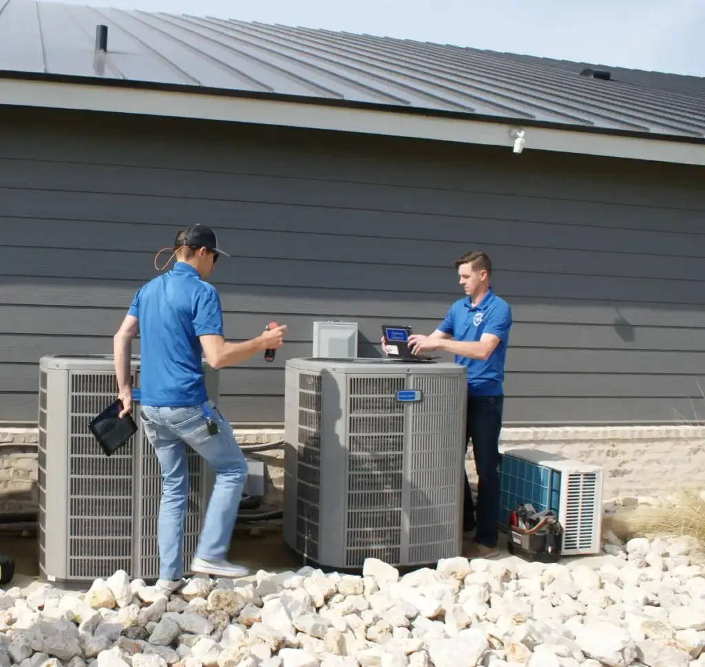 Two Murray technicians checking outdoor air-conditioning units beside a building