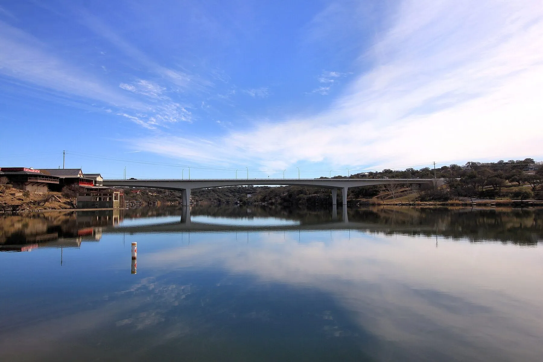 Calm Lake Marble Falls water with green shoreline and a low bridge