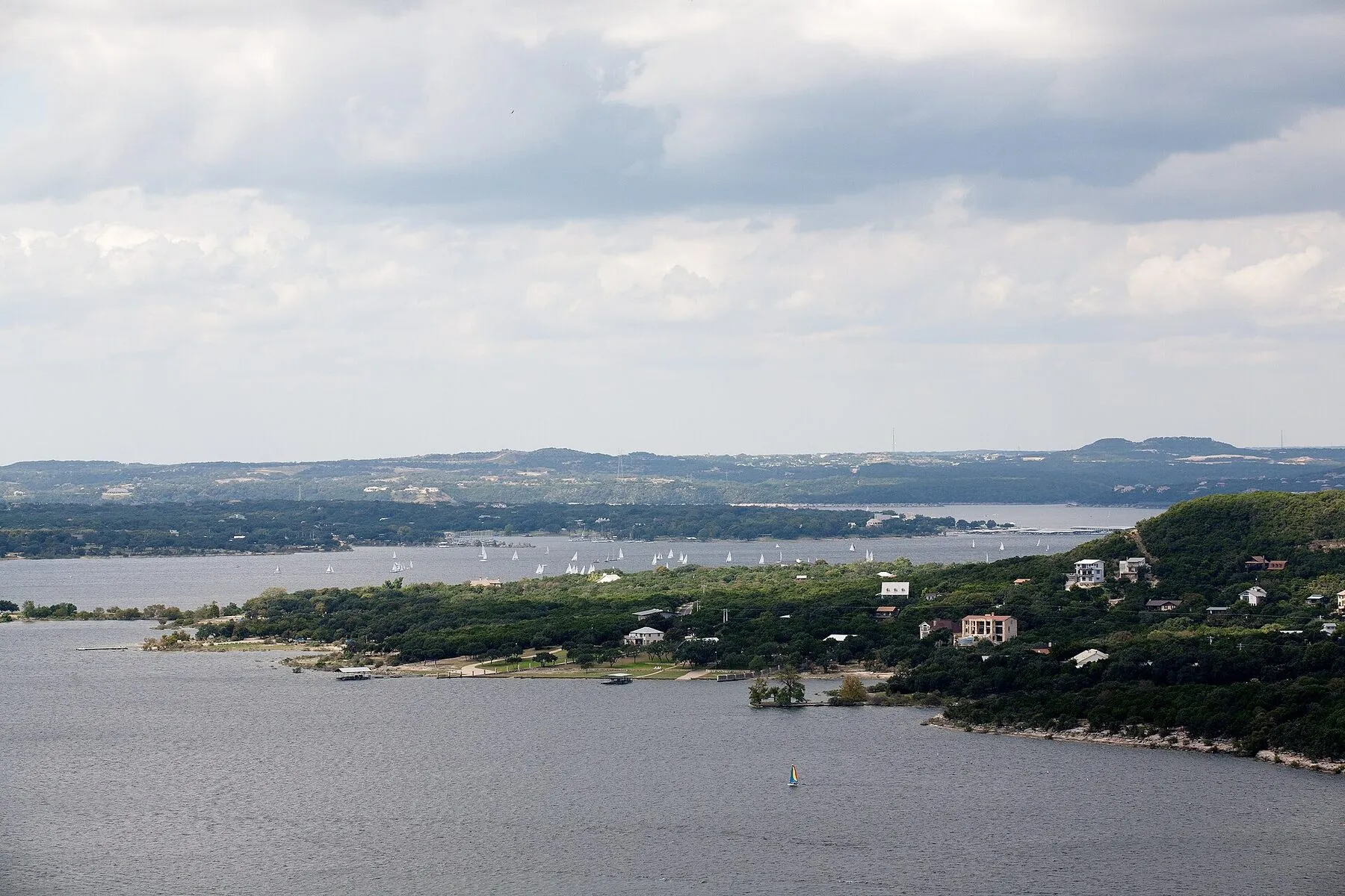 Blue Lake Travis water winding between green limestone hills