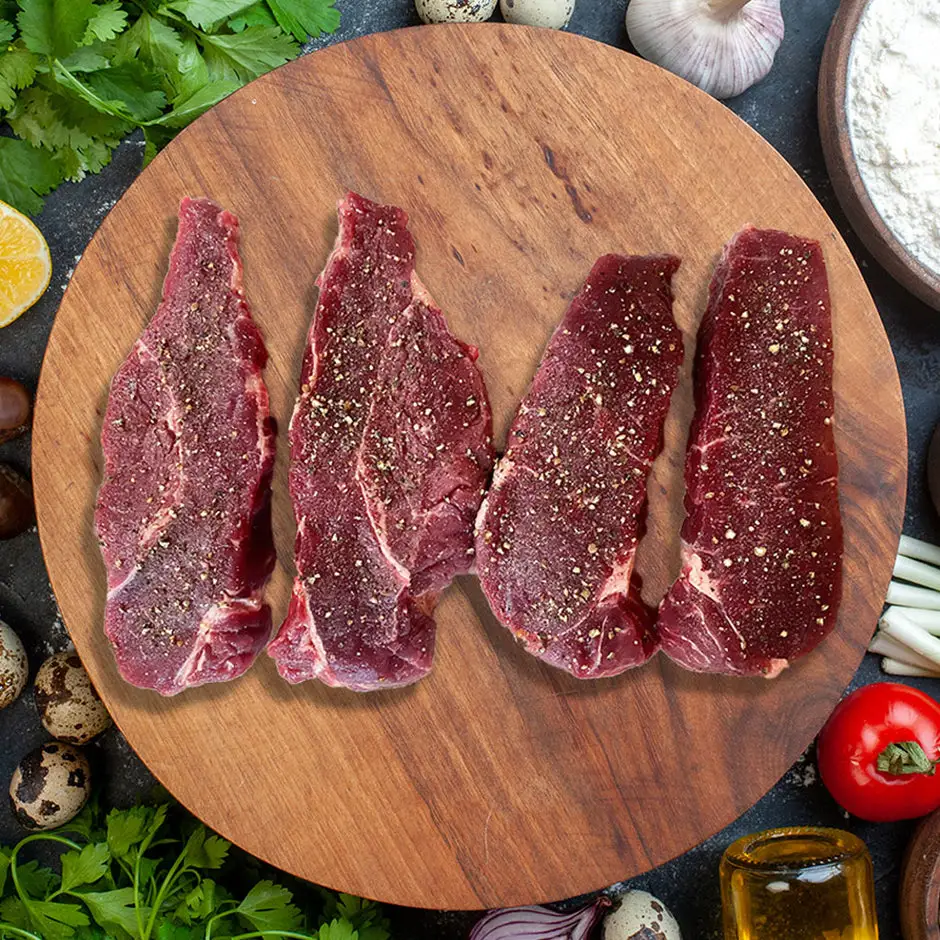 Four raw sirloin steaks on a wooden board with herbs