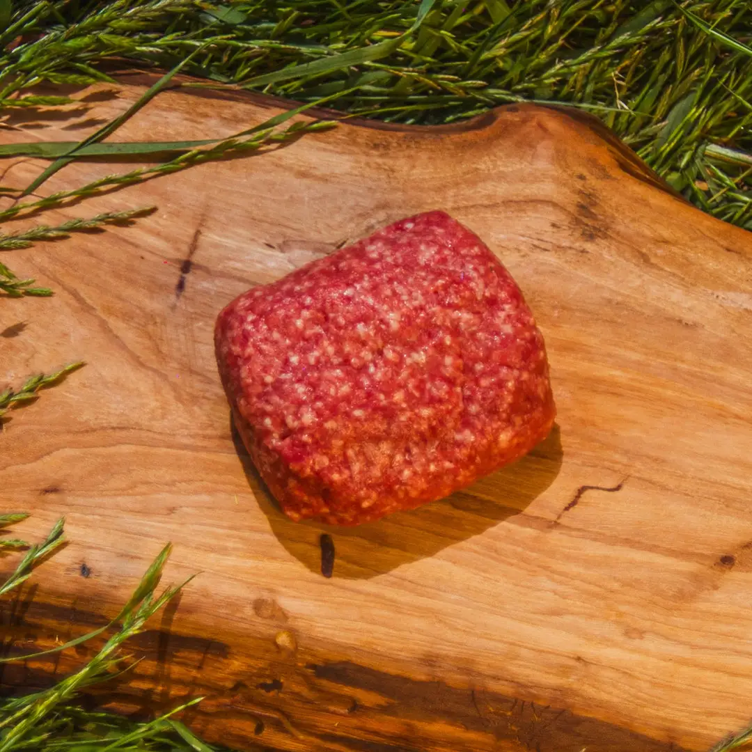 Raw ground beef on a wooden board surrounded by green grass stems