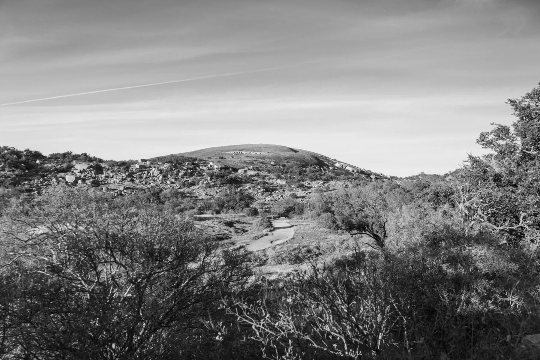 Black-and-white landscape with Enchanted Rock's rounded dome beyond scrub and boulders